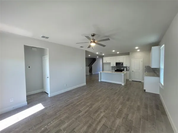 a view of an empty room with wooden floor and a kitchen