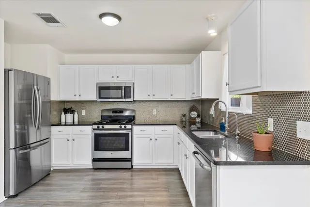a kitchen with stainless steel appliances granite countertop a refrigerator a stove top oven a sink dishwasher and white cabinets with wooden floor