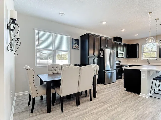 a kitchen with stainless steel appliances kitchen island granite countertop a refrigerator a stove a sink a dining table and chairs with wooden floor