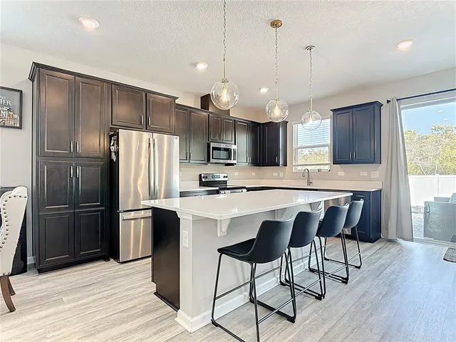 a kitchen with stainless steel appliances a refrigerator a sink a stove a kitchen island and chairs with wooden floor