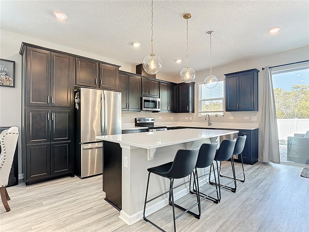 620 Grasshopper Ct Street St. Cloud, FL 34772 - Photo 8 of 29 a kitchen with stainless steel appliances a refrigerator a sink a stove a kitchen island and chairs with wooden floor