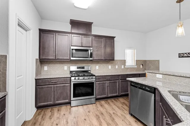 a kitchen with stainless steel appliances granite countertop a stove top oven a sink dishwasher a refrigerator and a microwave oven with wooden floor