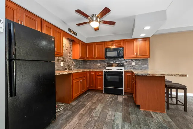 a kitchen with stainless steel appliances granite countertop a refrigerator a sink a stove and island with wooden floors