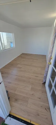 a view of an empty room with wooden floor and a window