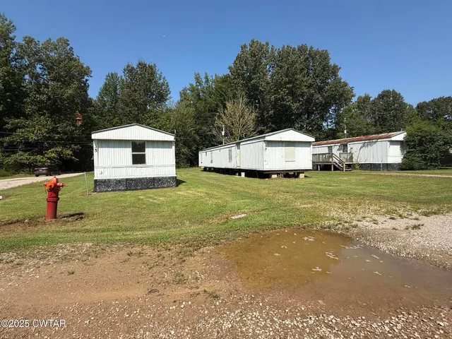 a white house with a big yard and large trees with wooden fence