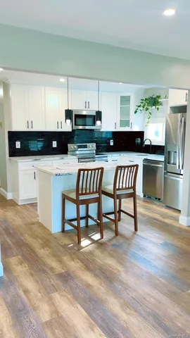 a kitchen with stainless steel appliances kitchen island granite countertop a refrigerator a stove a sink and white cabinets with wooden floor