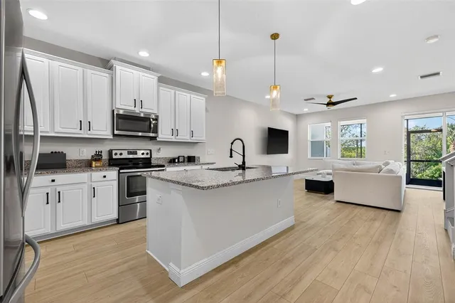 a large kitchen with stainless steel appliances kitchen island granite countertop a stove a sink a window and white cabinets