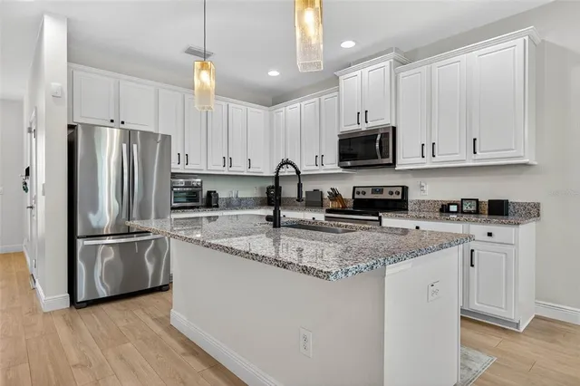 a kitchen with stainless steel appliances granite countertop a refrigerator stove a sink and white cabinets