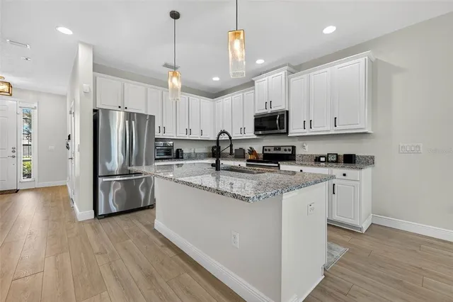 a kitchen with stainless steel appliances granite countertop a refrigerator a stove a sink and white cabinets with wooden floor