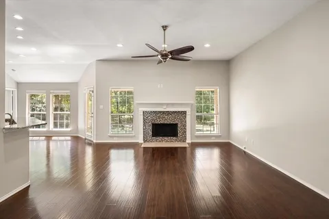 an empty room with wooden floor a ceiling fan a fireplace and windows