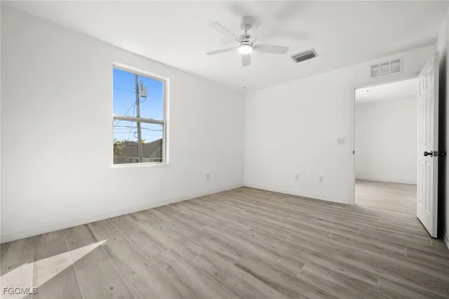 an empty room with wooden floor chandelier fan and windows