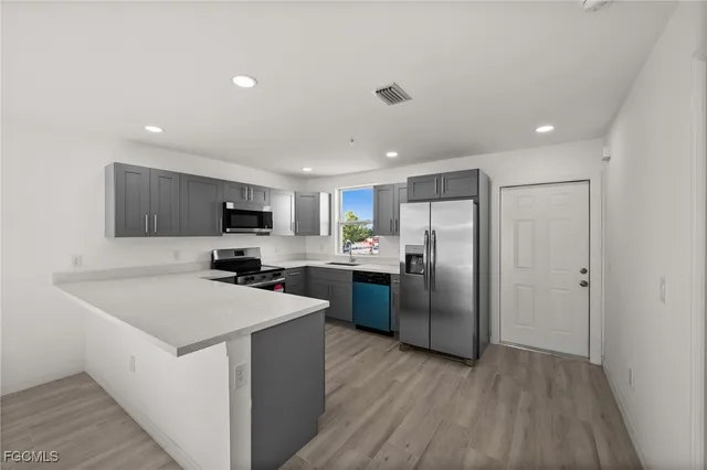 a kitchen with stainless steel appliances granite countertop a refrigerator a sink dishwasher a stove top oven a counter space and wooden floor