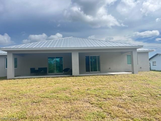 4414 Douglas Lane Lehigh Acres, FL 33973 - Photo 4 of 15 Rear view of property featuring a patio, stucco siding, a lawn, and a metal roof