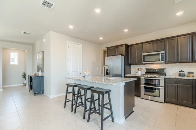 a kitchen with stainless steel appliances granite countertop a stove top oven a sink dishwasher a refrigerator and a dining table with wooden cabinet