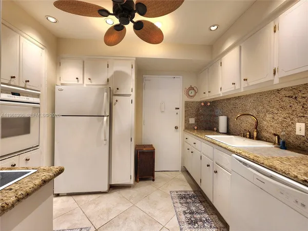a kitchen with stainless steel appliances granite countertop a refrigerator a sink and white cabinets