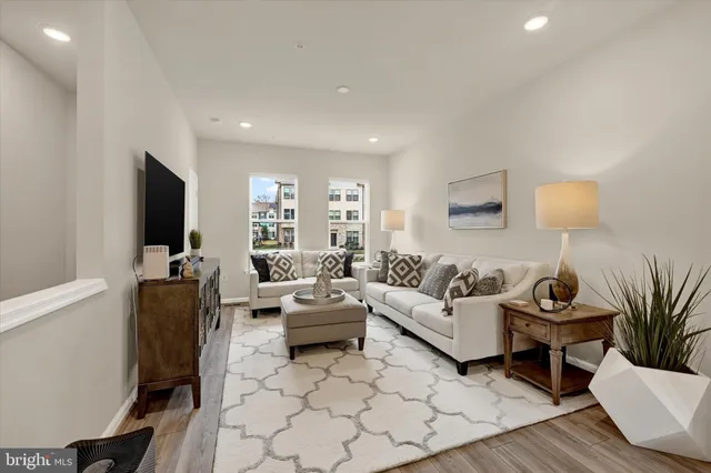 a kitchen with stainless steel appliances a stove a sink a refrigerator white cabinets and couches with wooden floor