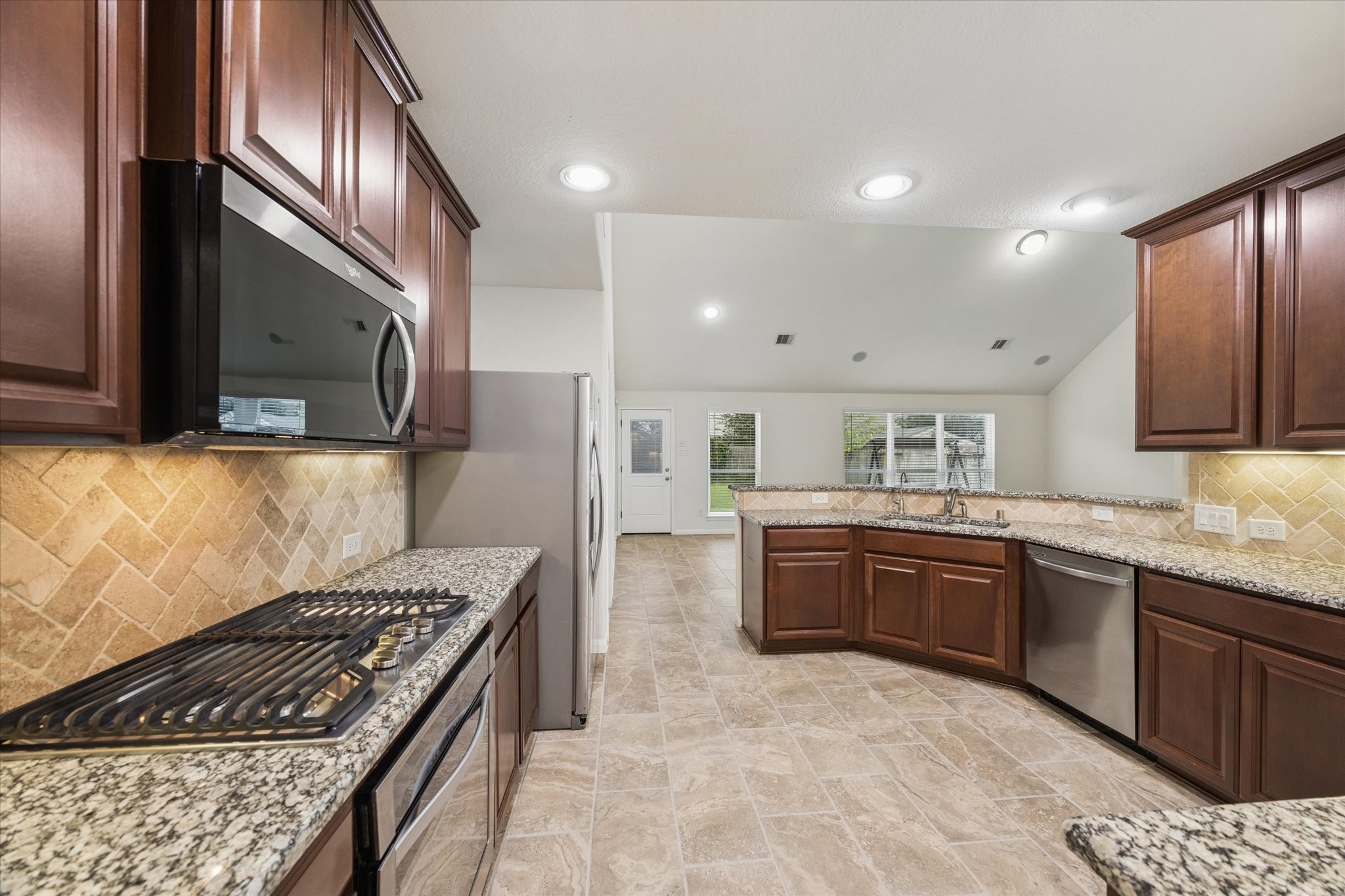 7015 Riata Hills Lane Spring, TX 77379 - Photo 12 of 33 This alternate view highlights the kitchen’s elegant travertine backsplash, perfectly coordinated with the tile flooring. A spacious gas cooktop enhances both the beauty and functionality of the space.