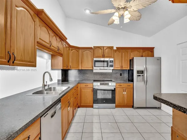 a kitchen with stainless steel appliances granite countertop a sink dishwasher stove and refrigerator with wooden cabinets