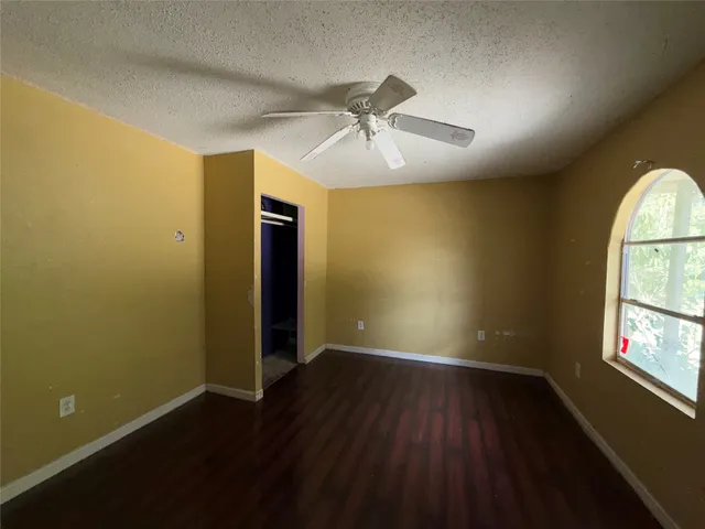 an empty room with wooden floor chandelier fan and windows