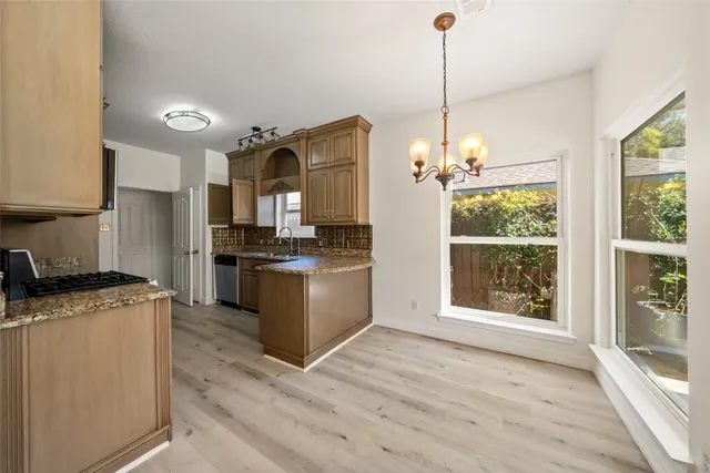 a kitchen with granite countertop a stove top oven a sink dishwasher a refrigerator and a dining table with wooden floor