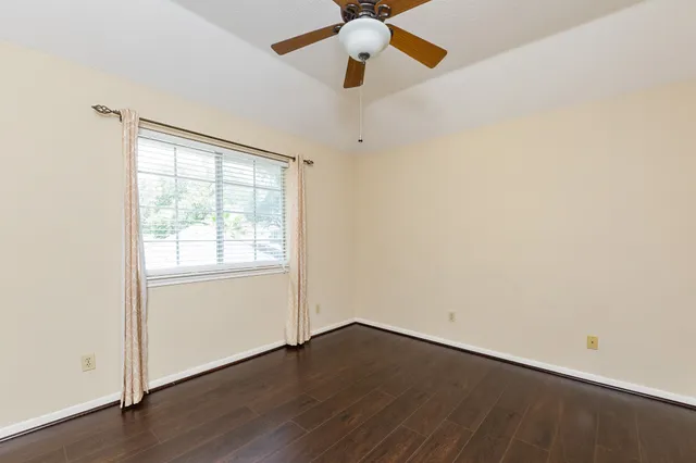 an empty room with wooden floor chandelier fan and windows