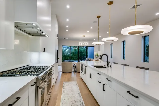 a kitchen with stainless steel appliances a stove a sink a chimney a large window and furniture