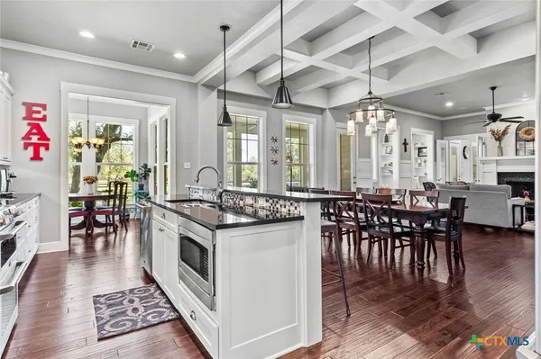 a kitchen with stainless steel appliances granite countertop a stove top oven a sink a dining table and chairs with wooden floor