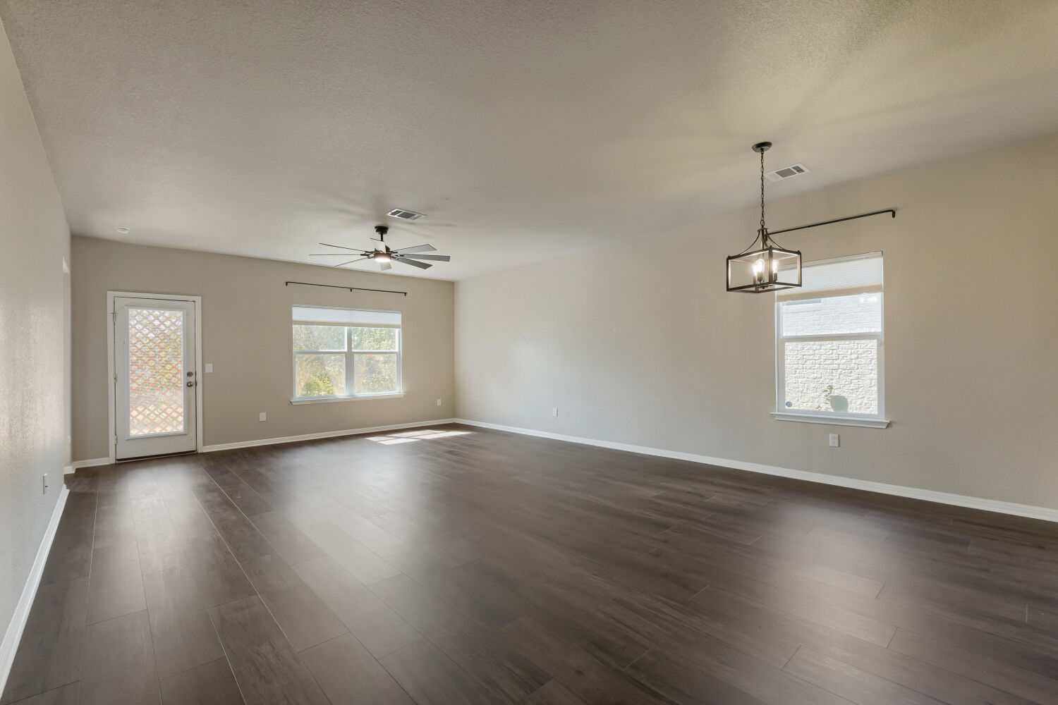Rich dark wood flooring stretches across this open living space with neutral walls.
