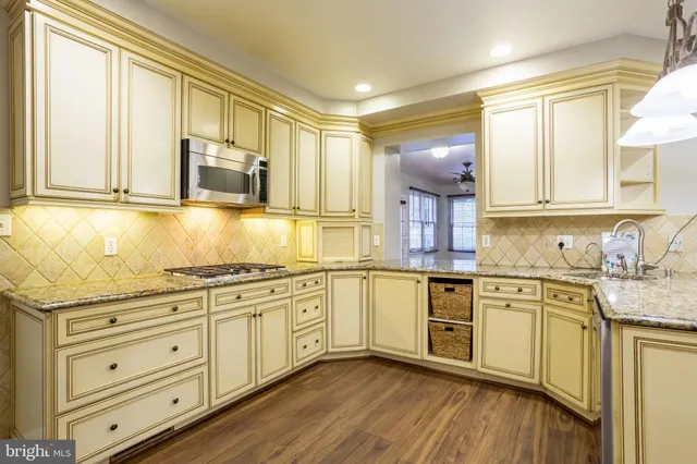 a kitchen with stainless steel appliances granite countertop a stove a sink dishwasher a refrigerator and white cabinets with wooden floor