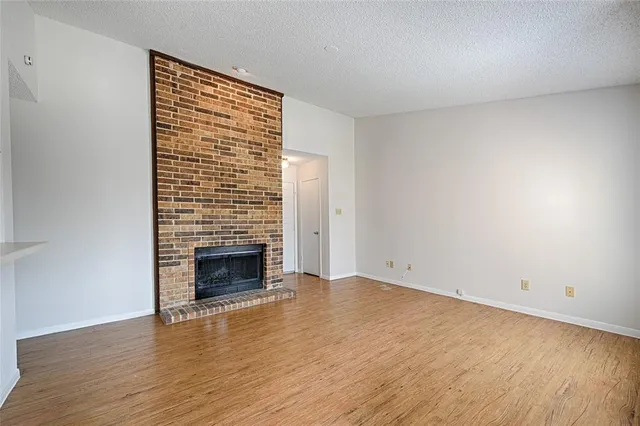 a view of an empty room with wooden floor fireplace and a window