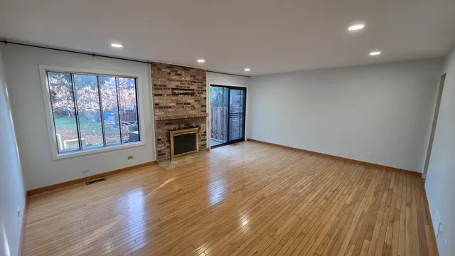 an empty room with wooden floor fireplace and windows