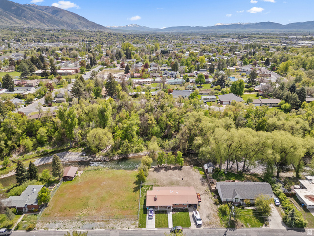 472 East 300 South Logan, UT 84321 - Photo 2 of 9 Aerial perspective showcasing a residential property with a brown roof and a paved driveway, featuring a verdant backdrop of mature trees and distant mountains