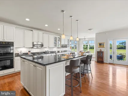 a kitchen with stainless steel appliances granite countertop a stove top oven a sink a refrigerator and white cabinets with wooden floor