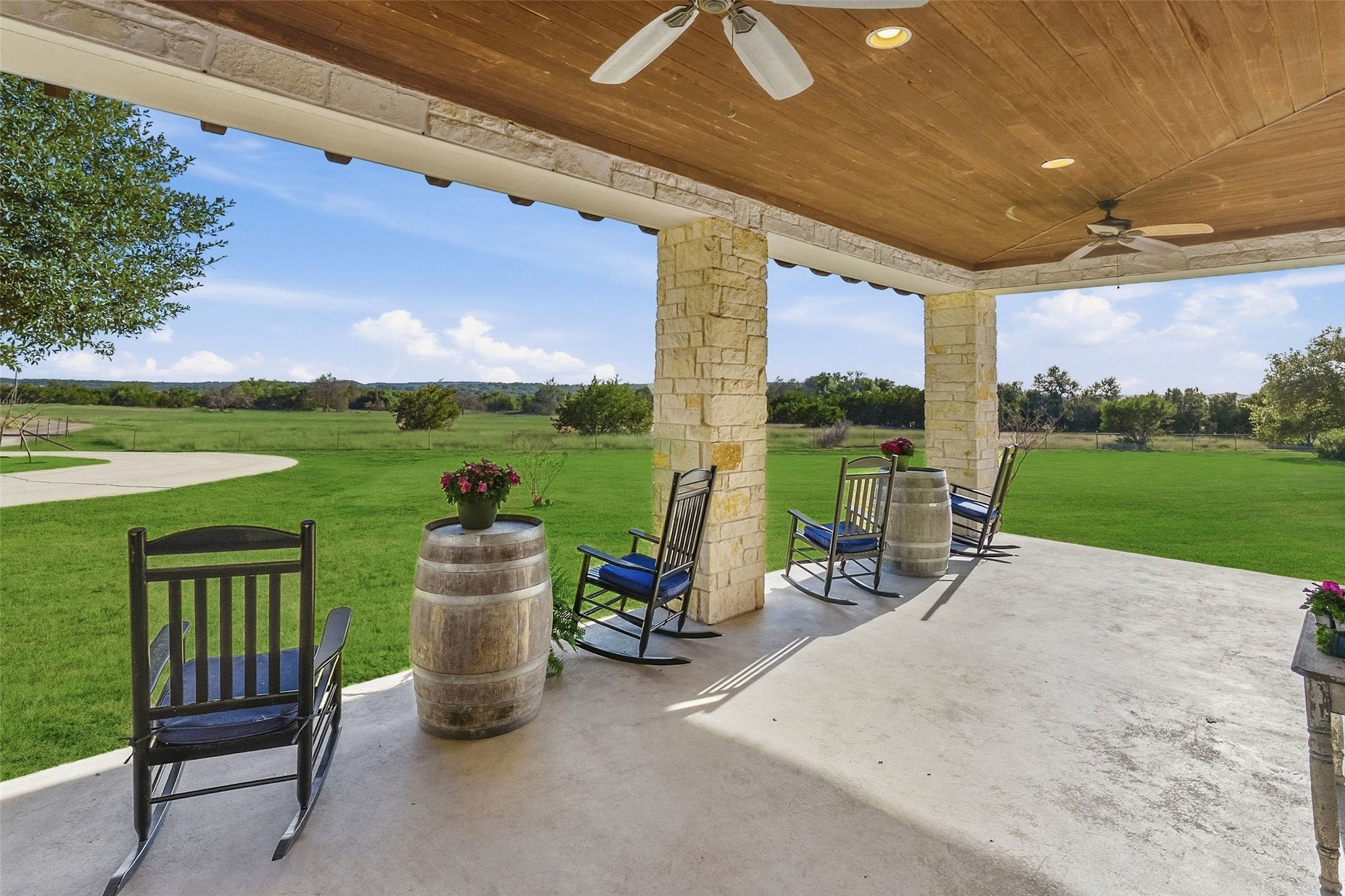 7220 Creek Road Dripping Springs, TX 78620 - Photo 2 of 40 A spacious covered patio features warm wood ceilings, stone pillars, and sweeping lawn views.