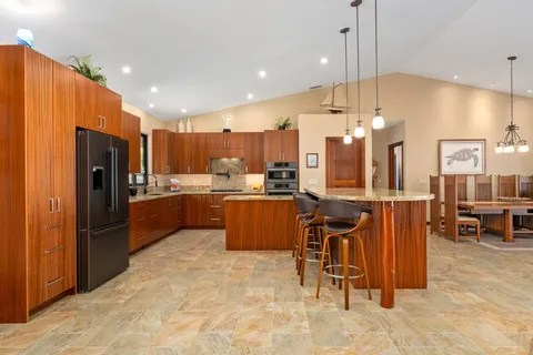 a kitchen with stainless steel appliances kitchen island granite countertop a refrigerator a oven a sink a island and chairs with wooden floor