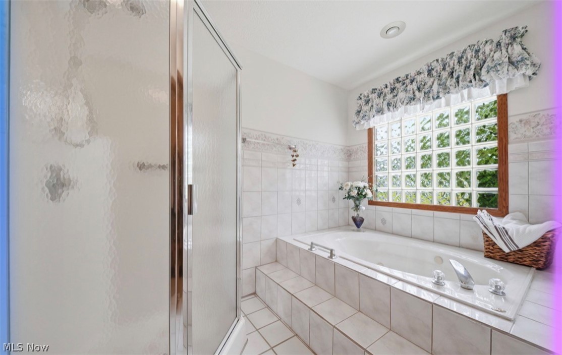 3556 Lake Road Conneaut, OH 44030 - Photo 9 of 39 White tiled bathroom featuring a built-in soaking tub with tiered steps, a glass block window with wood trim, and a separate shower enclosure with textured glass panels and chrome framing