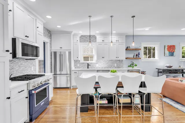 a kitchen with stainless steel appliances kitchen island granite countertop a sink a stove a refrigerator and chairs