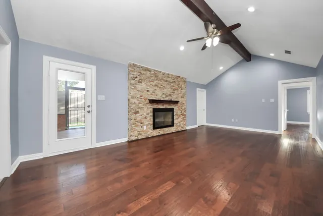 an empty room with wooden floor fireplace and windows