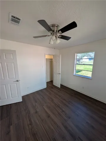 a view of an empty room with wooden floor and a ceiling fan