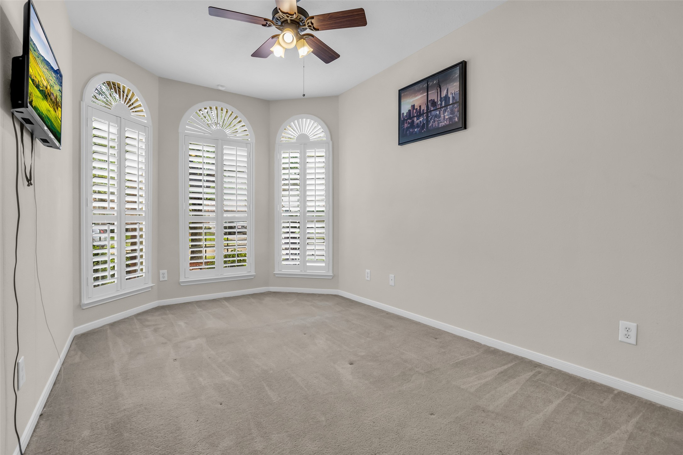 6807 Chapelfield Lane Houston, TX 77049 - Photo 30 of 42 This room features large arched windows with plantation shutters, providing ample natural light. It includes a ceiling fan, neutral carpet, and walls, perfect for a cozy bedroom or office.