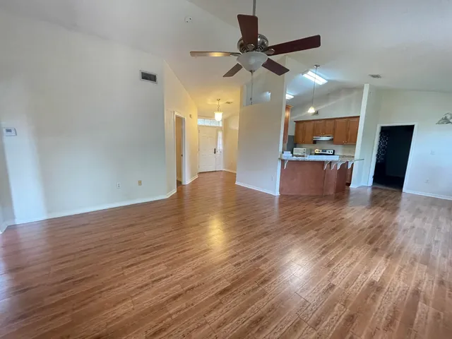 a view of a room with wooden floor a ceiling fan and kitchen space