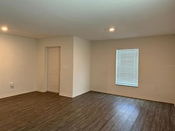 a view of an empty room with wooden floor and a window
