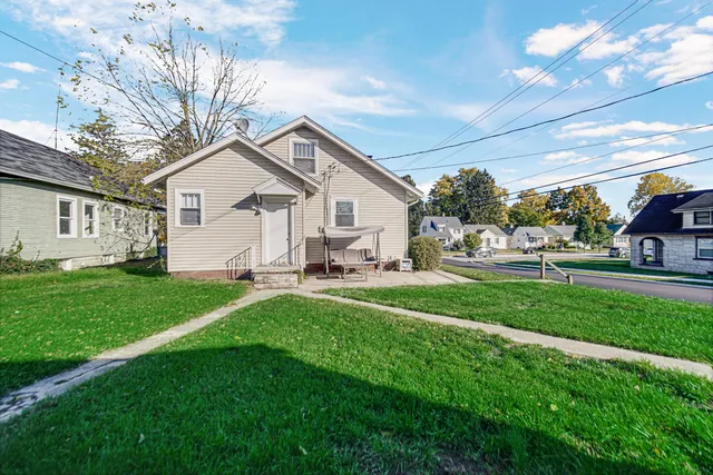 a view of a white house in front of a yard with lawn chairs and a big yard