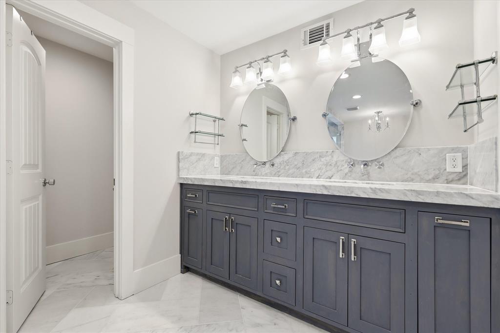 4310 Forest Bend Road Dallas, TX 75244 - Photo 19 of 40 Double vanity with dark wood cabinetry, light stone countertop, oval mirrors, and wall-mounted lighting fixtures