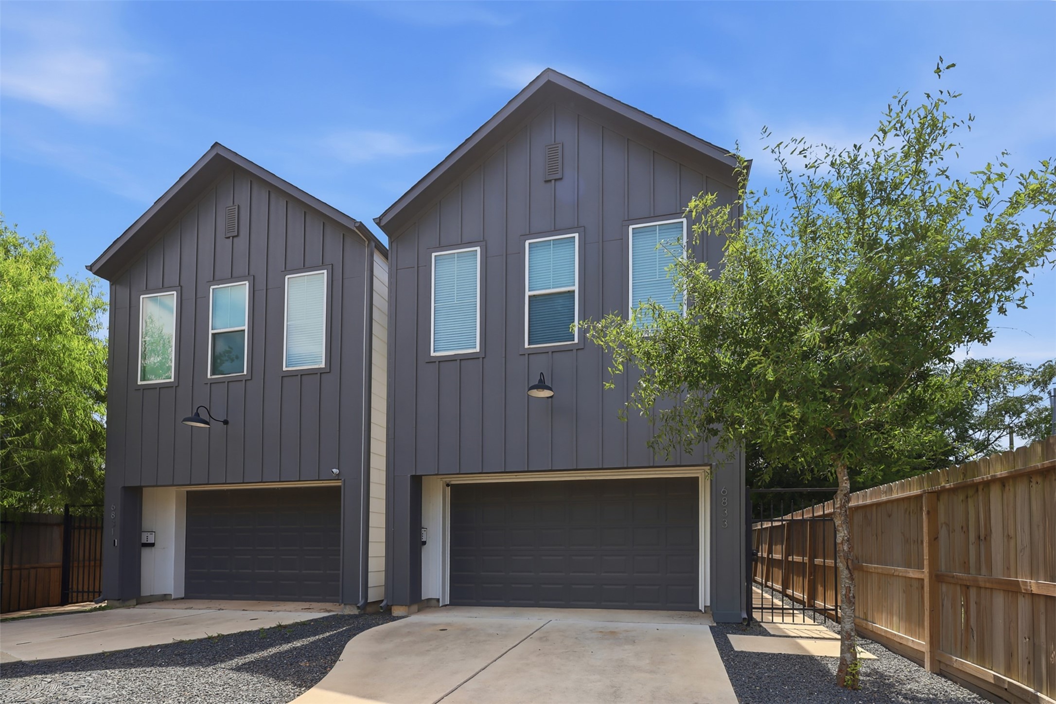 6833 Paris Street Houston, TX 77021 - Photo 1 of 23 Modern duplex with a sleek dark exterior, featuring two garages and a shared driveway. The property is fenced and landscaped with trees for added privacy.