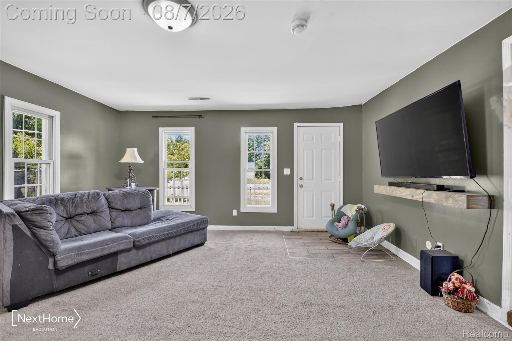23740 Carleton West Road Belleville, MI 48111 - Photo 12 of 58 Spacious room featuring neutral wall paint, light-colored carpeting, multiple windows with white trim, a white door, and a wall-mounted wood-finish shelf