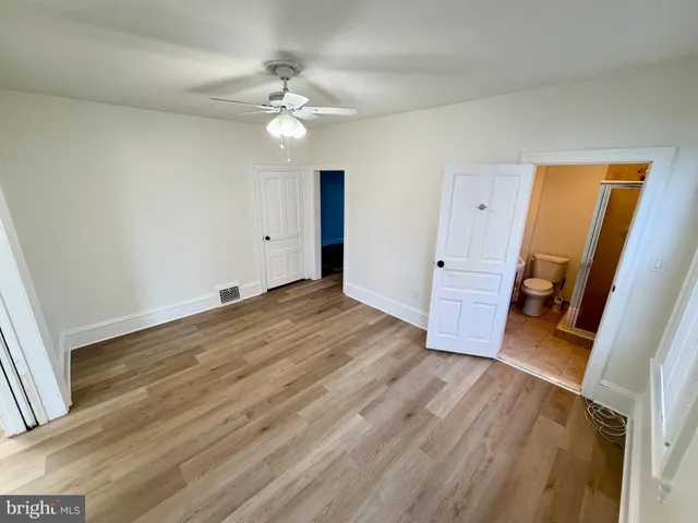 a view of an empty room with wooden floor and a ceiling fan