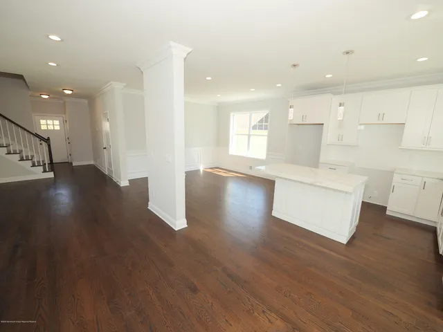 a view of an empty room and kitchen with wooden floor