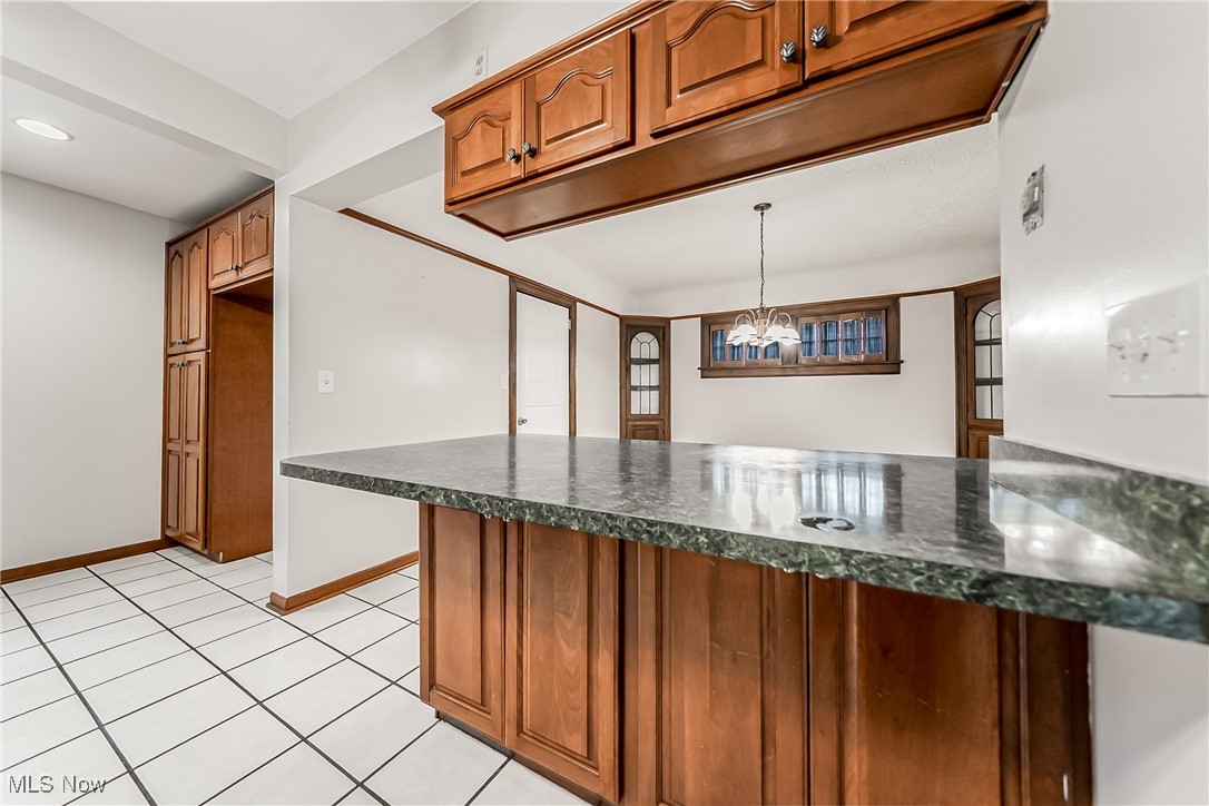 1271 Winston Road Cleveland, OH 44121 - Photo 13 of 43 Kitchen with brown cabinetry, a peninsula, light tile patterned floors, and a chandelier