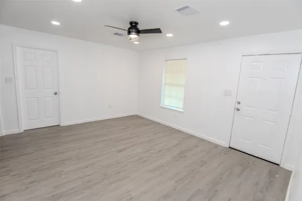 an empty room with wooden floor fan and windows